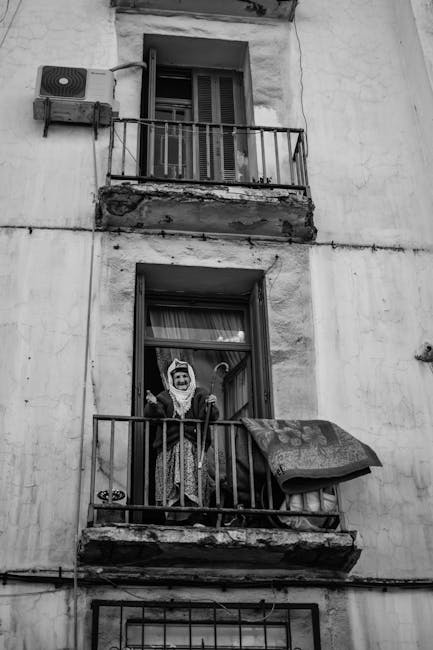 Black and white photo of an elderly woman standing on a balcony in Algeria.