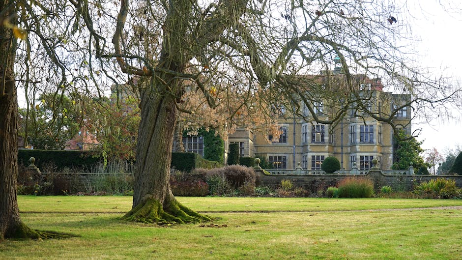 A historic mansion in the English countryside with lush greenery and mature trees.